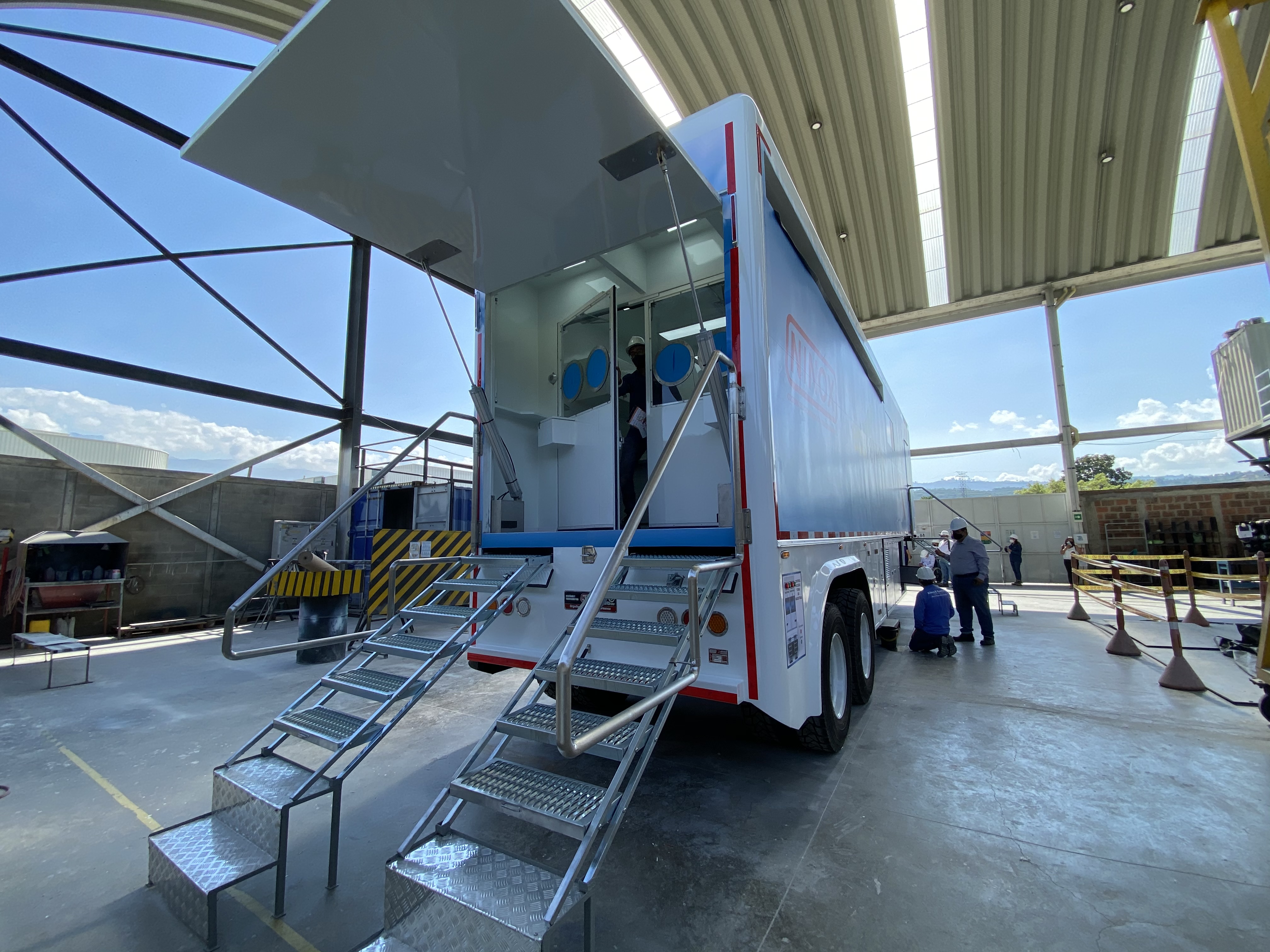 Interior of the LAB BIO MAX biological waste management area: red hazardous waste container, social distancing signage, and sample pass-through window between zones. Every element answers to a specific biosafety requirement.