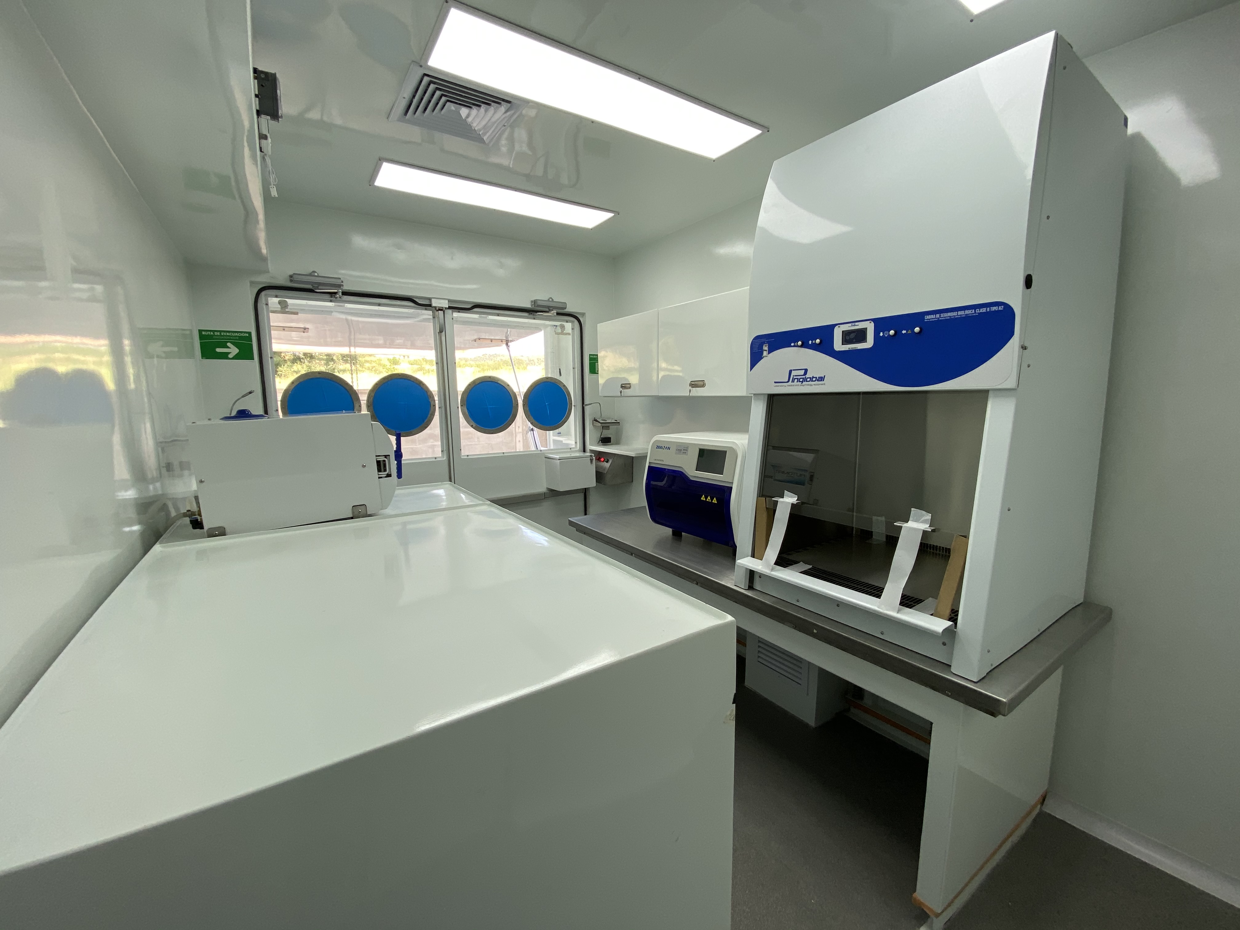 Interior module view: flush-mounted circular LED panels, germicidal UV tube, and industrial lever-lock storage cabinets. The clean geometry eliminates surfaces that are difficult to decontaminate.