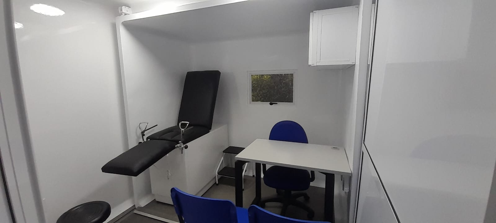 The consultation room: articulated exam table, physician's desk, and patient seating — a complete clinical space compressed with precision engineering.