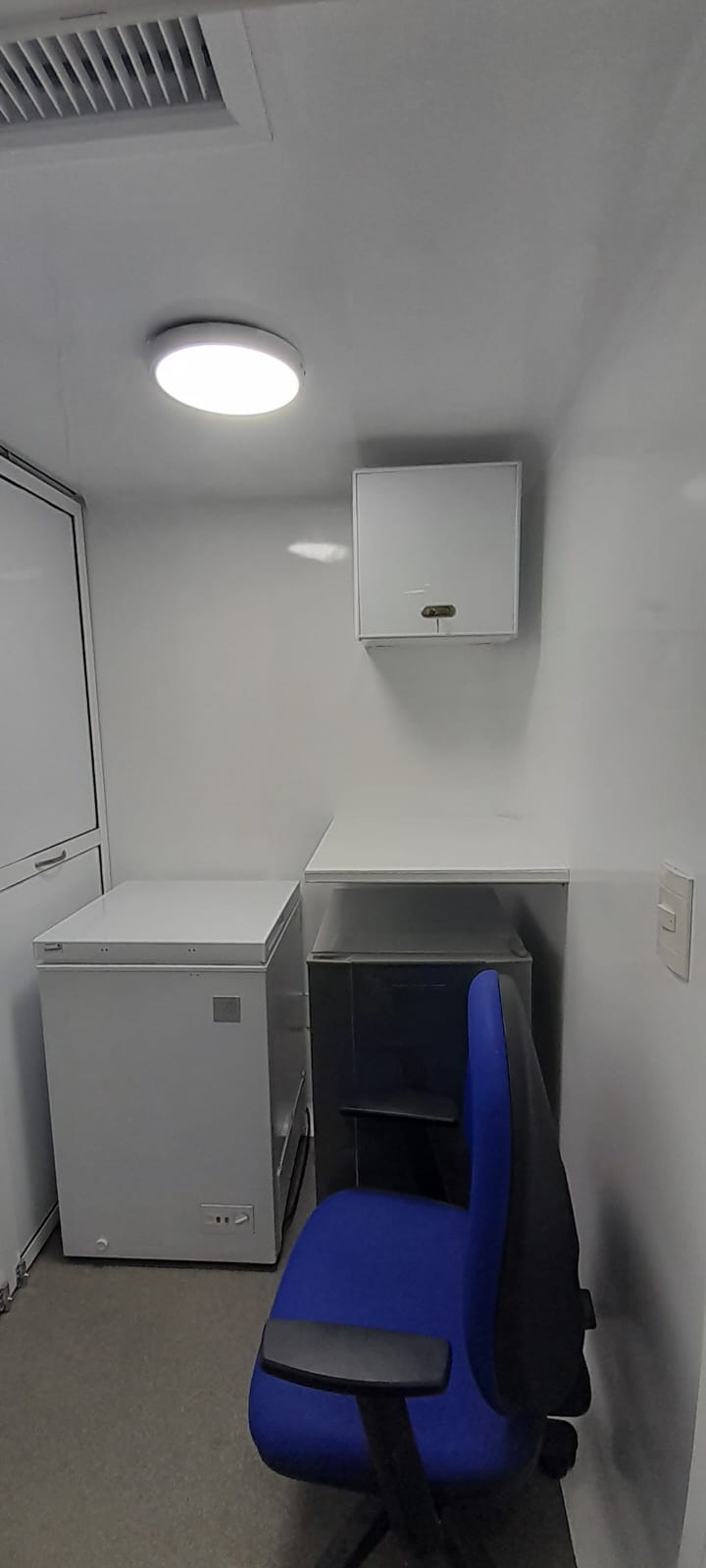 Sample storage and work area, featuring a chest refrigerator, laboratory countertop, and overhead medical supply cabinet.